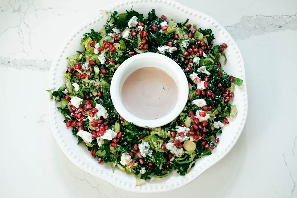 Large plate of salad with pomegranate seeds and homemade dressing in the middle 