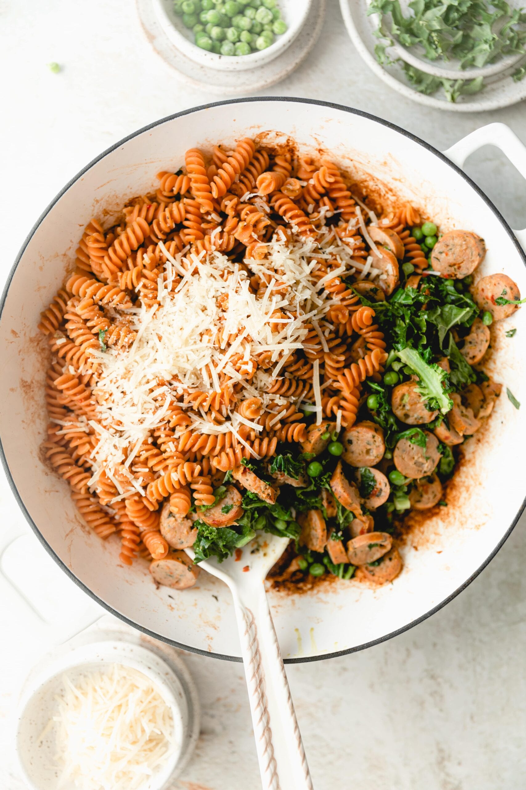 white skillet with pasta, chicken sausage, kale, and peas topped with parmesan cheese