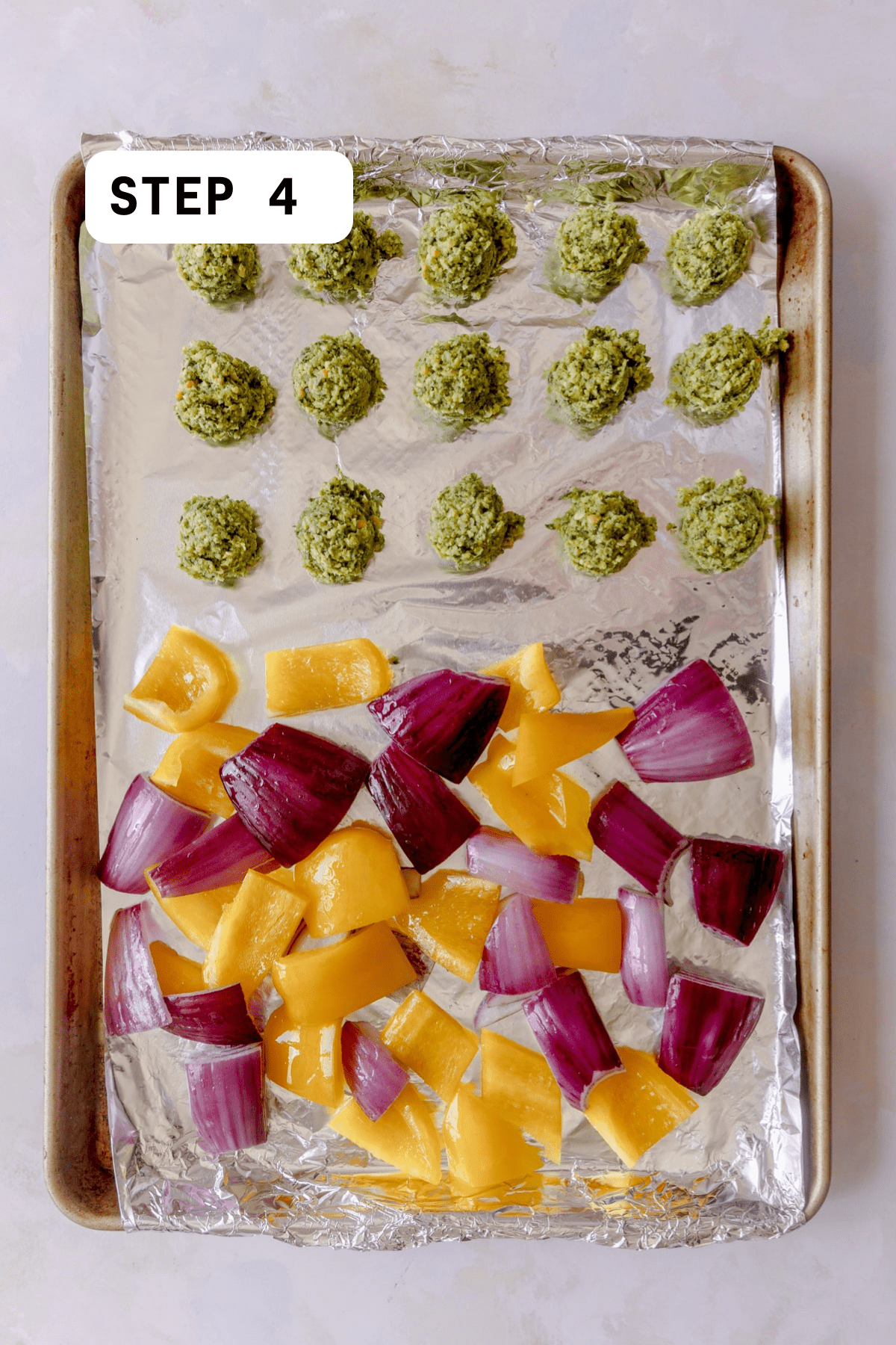 Falafel balls, peppers, and onions on a foil lined baking tray.  