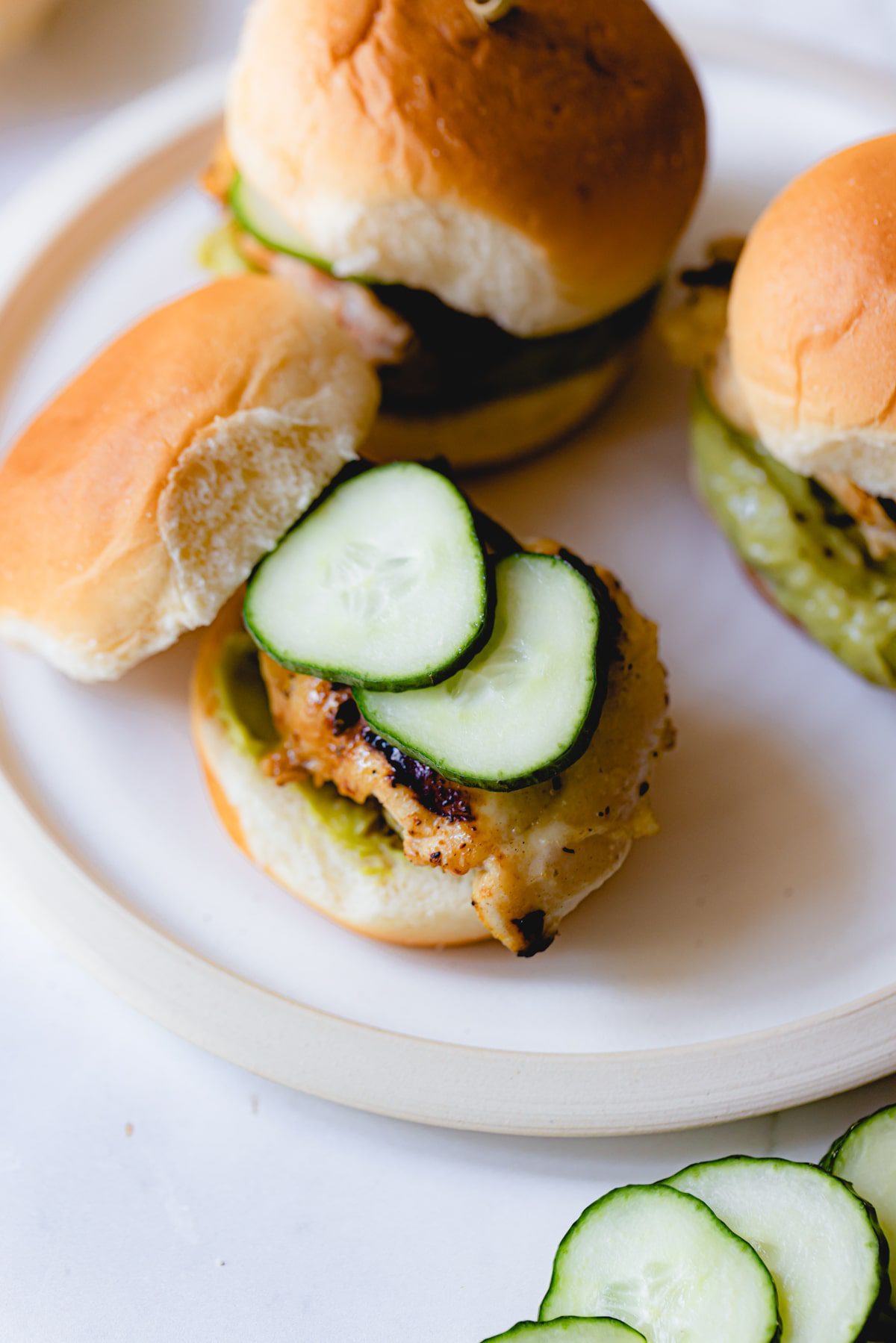 An assembled chicken slider on Hawaiian roll topped with cucumber. 