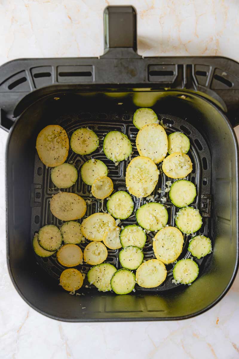 Air fryer basket with zucchini slices. 