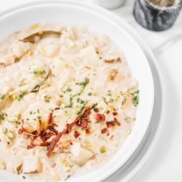 Clam chowder in a white bowl with bacon and chive topping