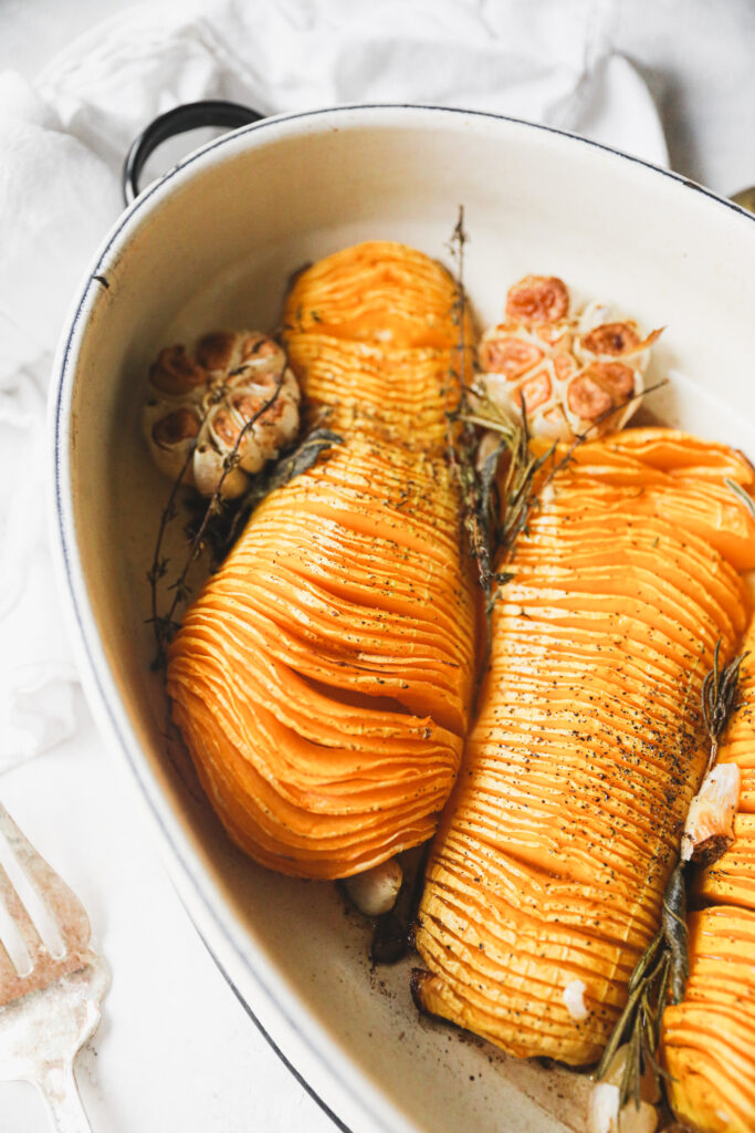 hasselback squash in a roasting pan with garlic and herbs