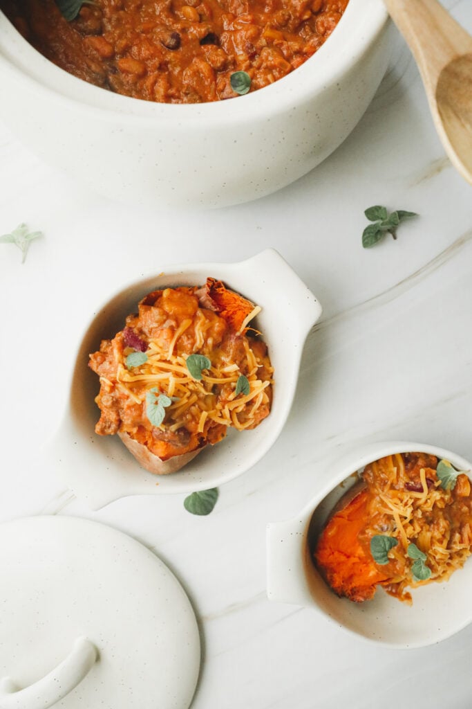 2 bowls of creamy pumpkin chili over sweet potatoes. Garnished with fresh oregano.