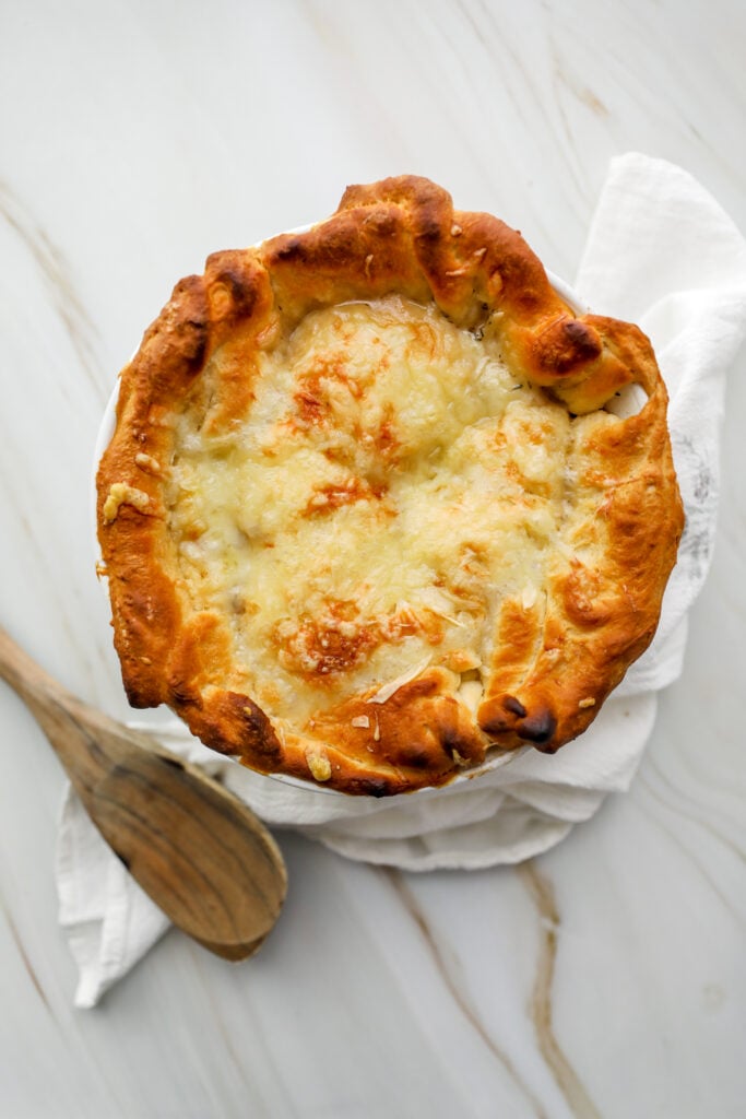 top down shot of French onion pot pie with wooden spoon and white linen