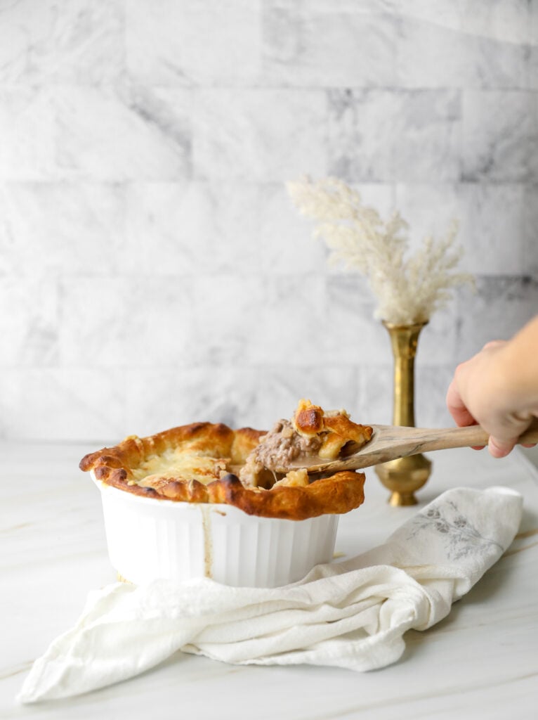 wooden spoon dipping into a hot beef and onion pot pie
