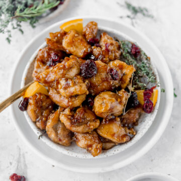 cranberry orange chicken on white plates surrounded by dried thyme and cranberries