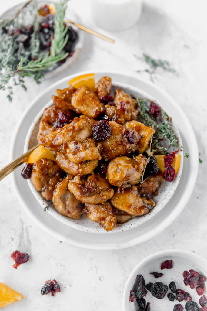 cranberry orange chicken on white plates surrounded by dried thyme and cranberries