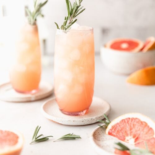 2 Moscow mules in pink clear cups surrounded by grapefruit and rosemary garnish