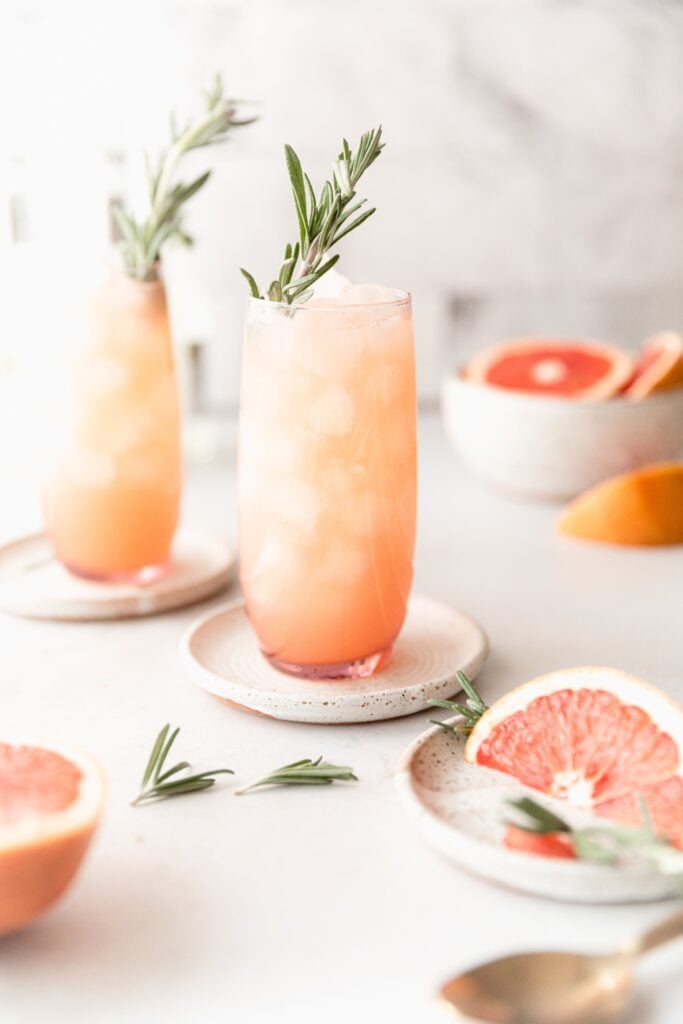 2 Moscow mules in pink clear cups surrounded by grapefruit and rosemary garnish