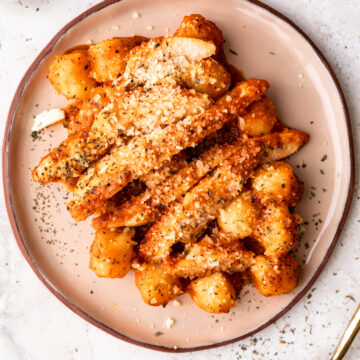 Roasted red pepper chicken and gnocchi on a beige plate with a gold fork