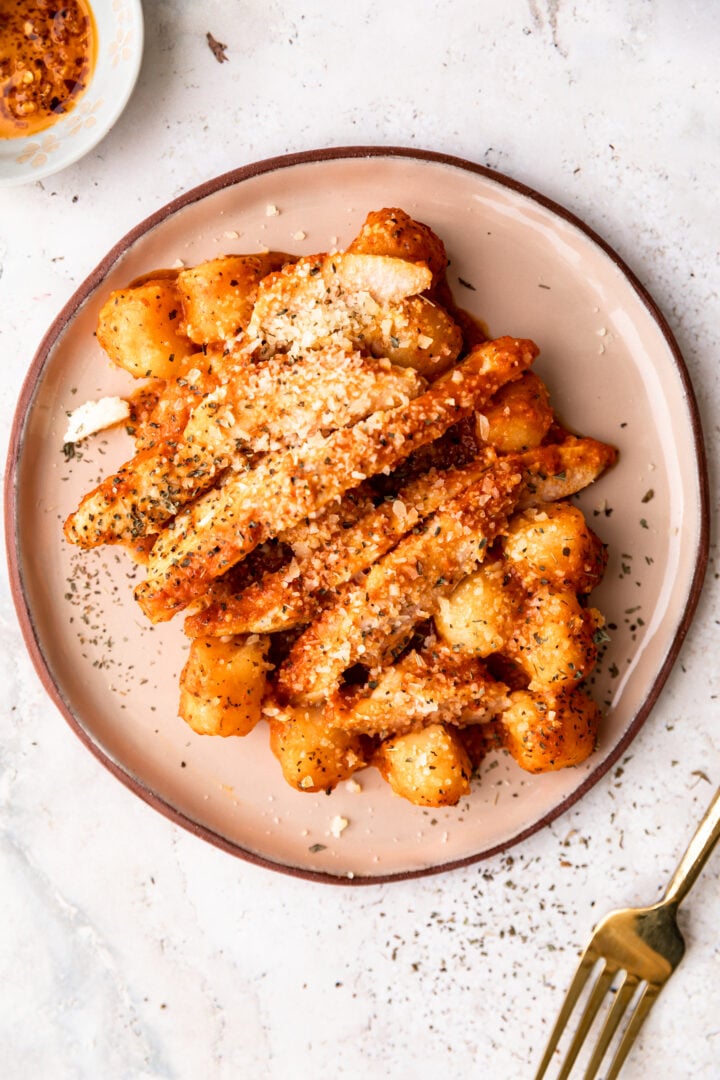 Roasted red pepper chicken and gnocchi on a beige plate with a gold fork