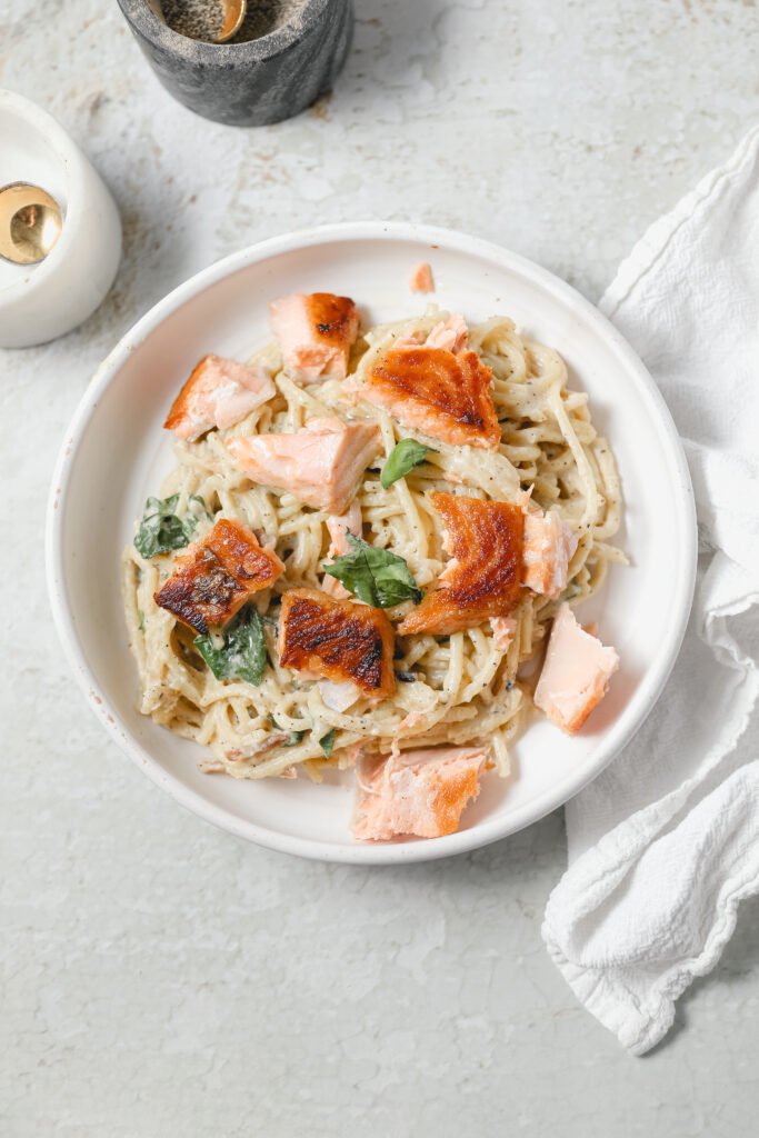 bowl of salmon spinach pasta in a white dish with white linen 
