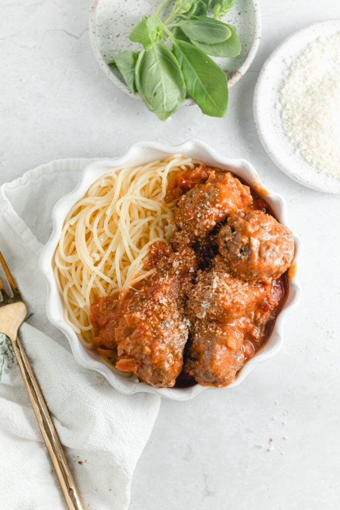 bowl of spaghetti and vodka sauce covered meatballs. Surrounded by fresh basil and parmesan cheese 
