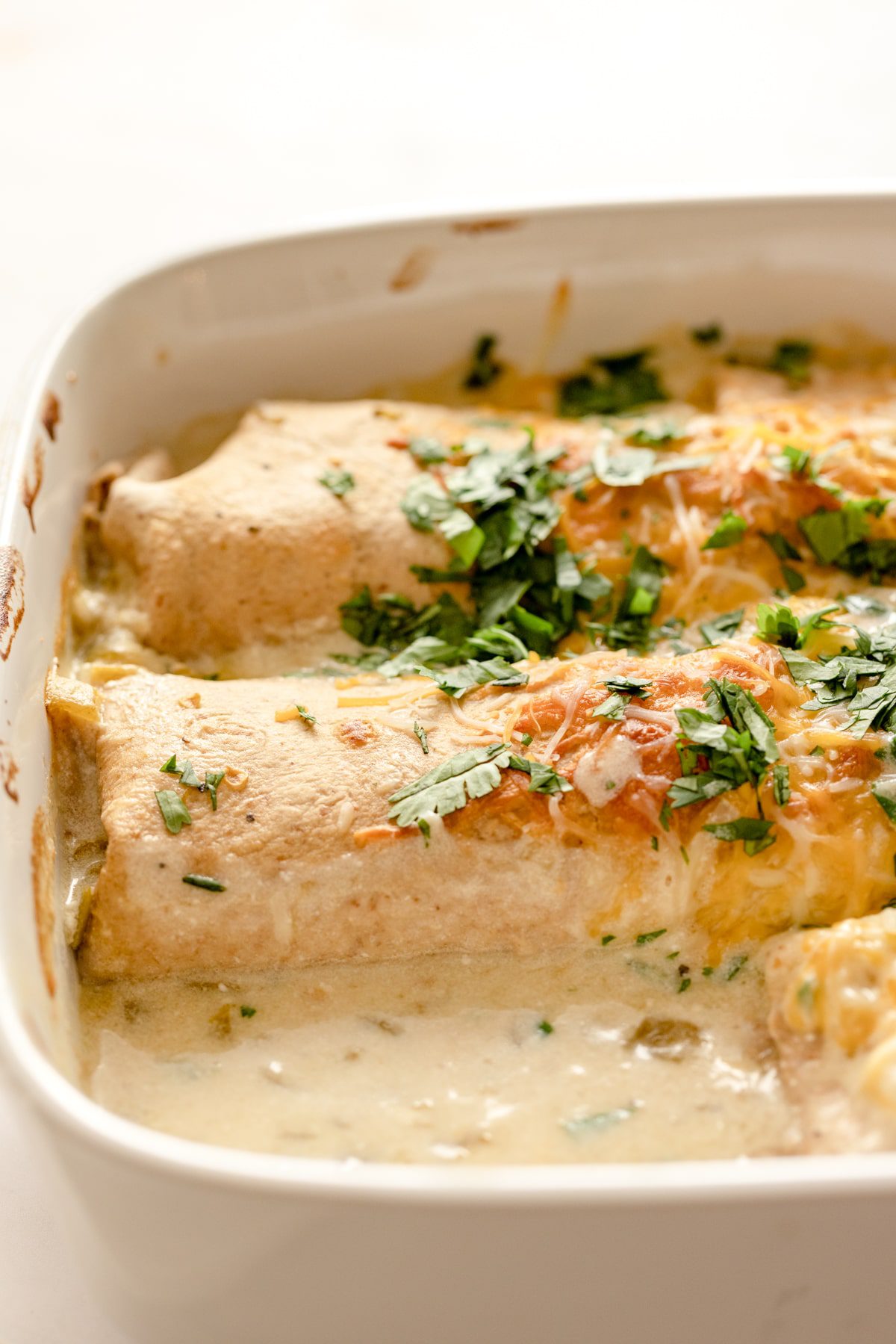 white chicken enchiladas baked in a dish with one removed.