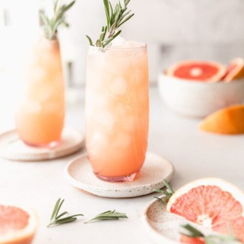 2 Moscow mules in pink clear cups surrounded by grapefruit and rosemary garnish