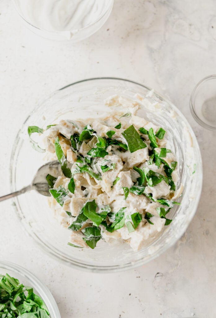 glass bowl with mixed spinach artichoke chicken salad
