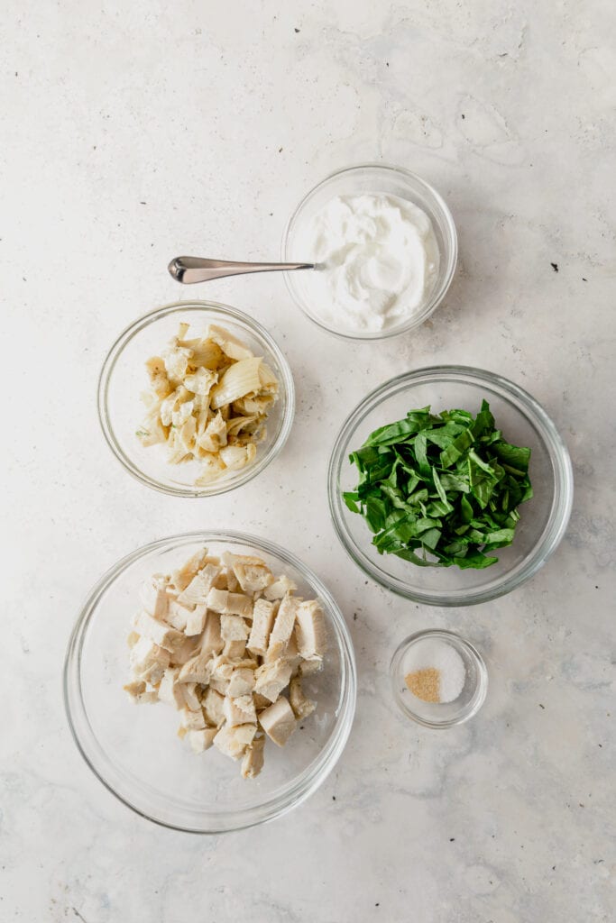 glass bowls with ingredients for spinach artichoke chicken salad. 