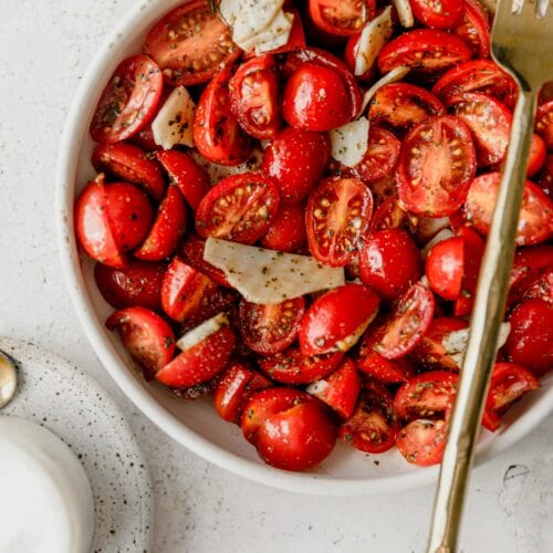 white bowl full of cherry tomatoes in Italian marinade with a gold fork