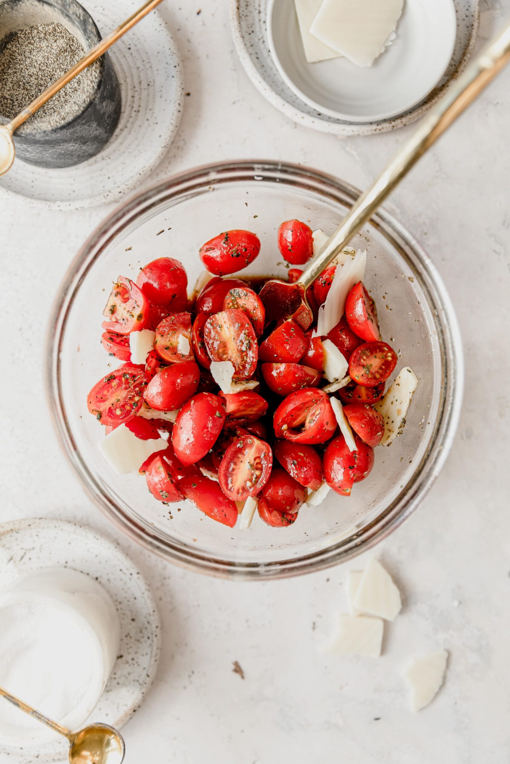 mixing tomatoes and balsamic Italian marinade in a clear glass bowl with a gold fork 
