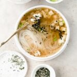 white bowl of miso soup with garnishes arranged around
