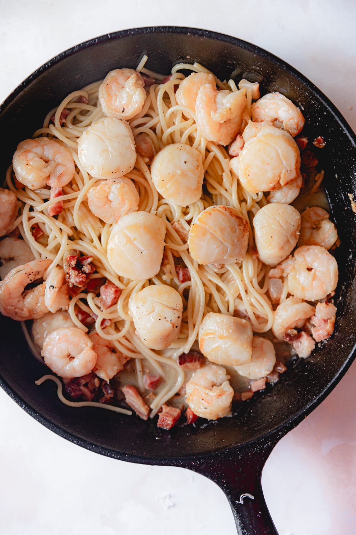 Pasta added to shrimp and scallops in a skillet. 