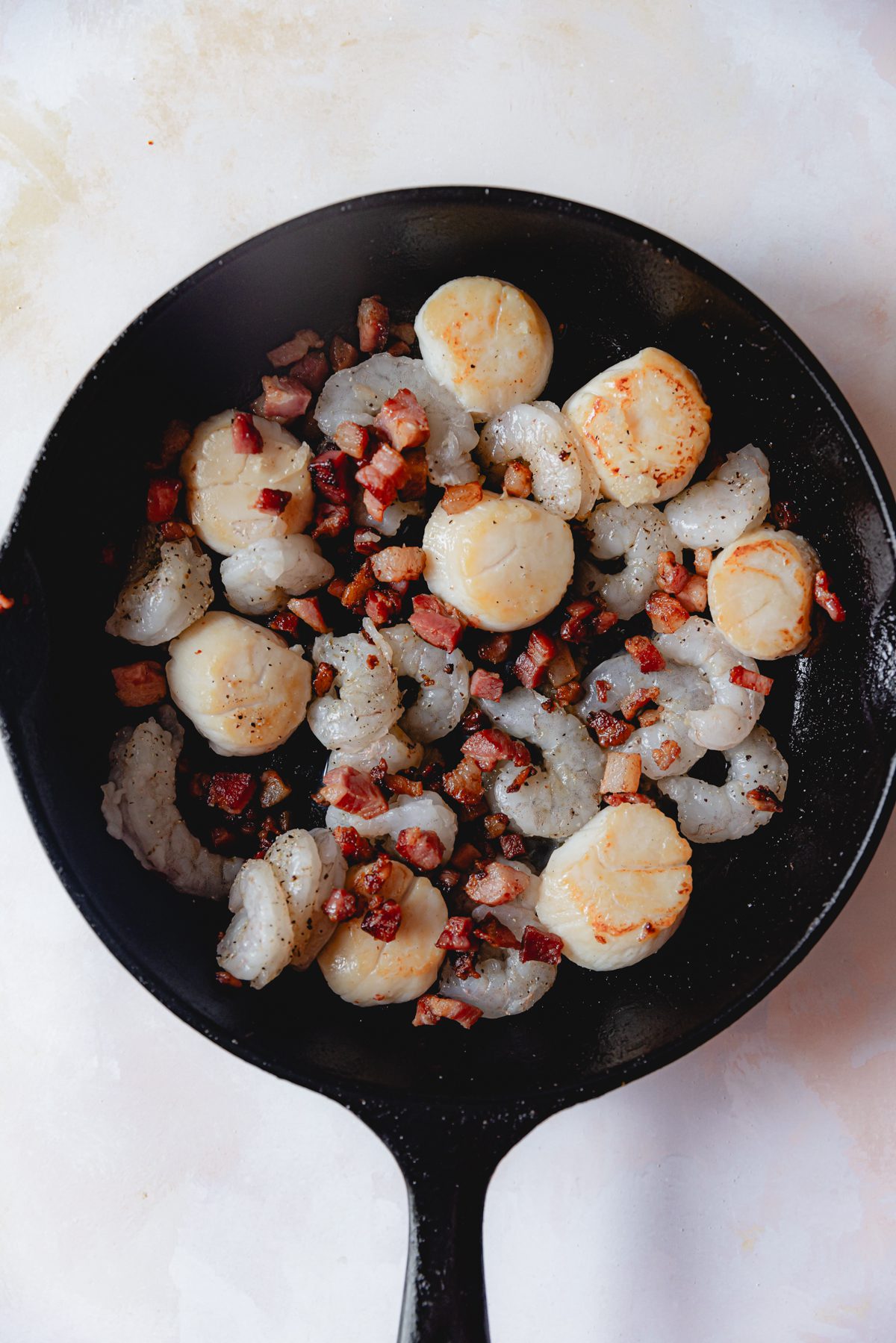 Shrimp, scallops, and pancetta cooking in a cast iron skillet. 