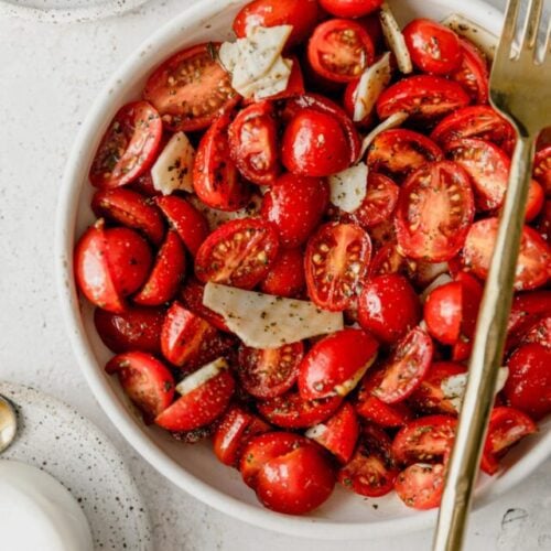 white bowl full of cherry tomatoes in Italian marinade with a gold fork