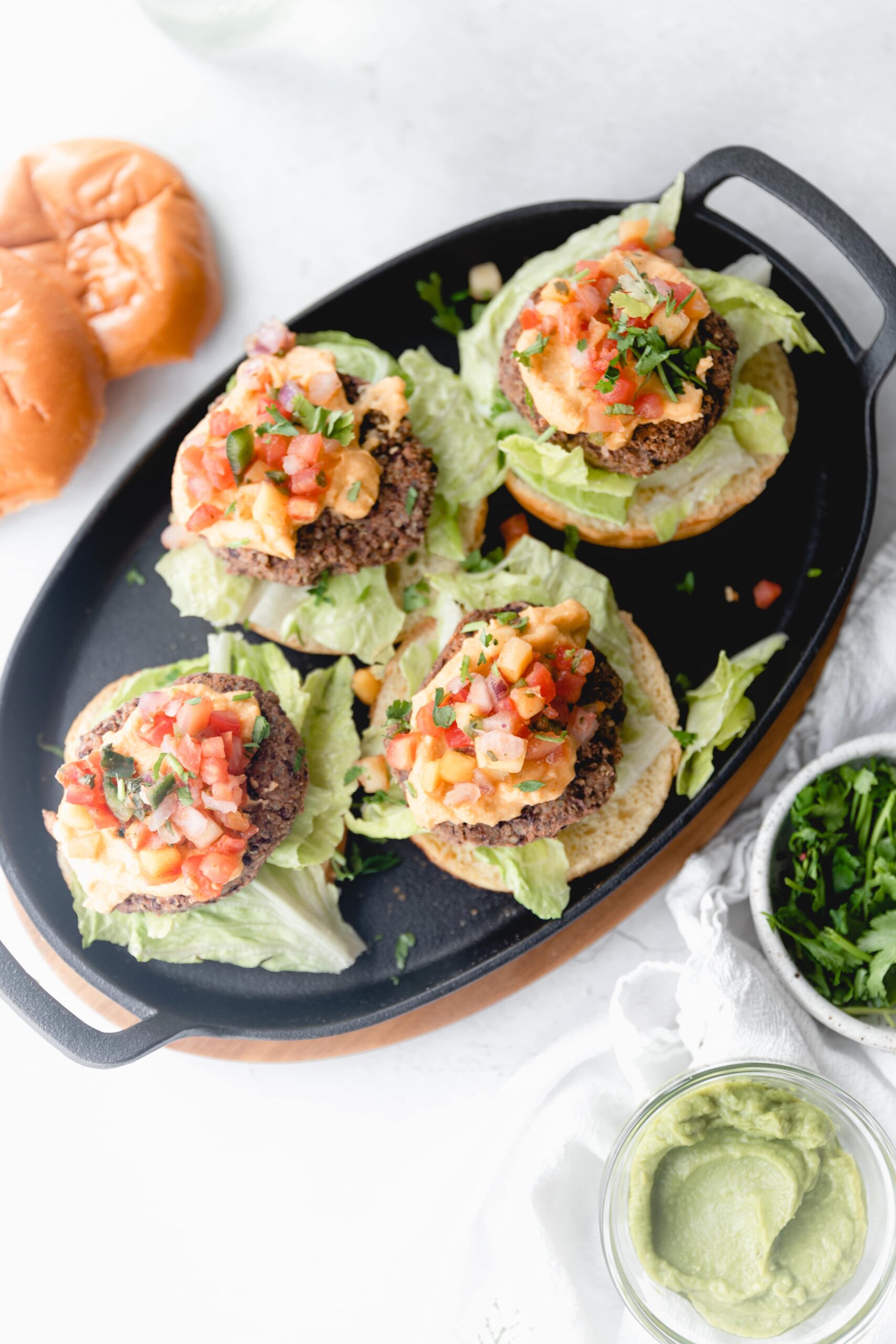 overhead shot of 4 open faced black bean nacho burgers on a black skillet