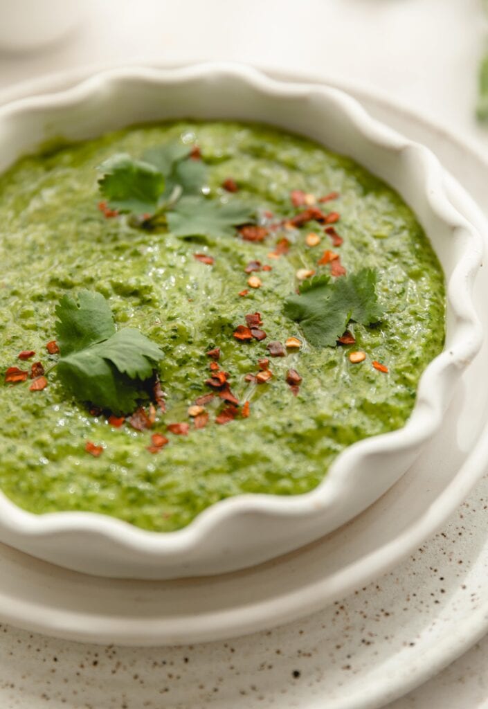 white bowl full of cilantro chimmichurri garnished with cilantro and red pepper flakes
