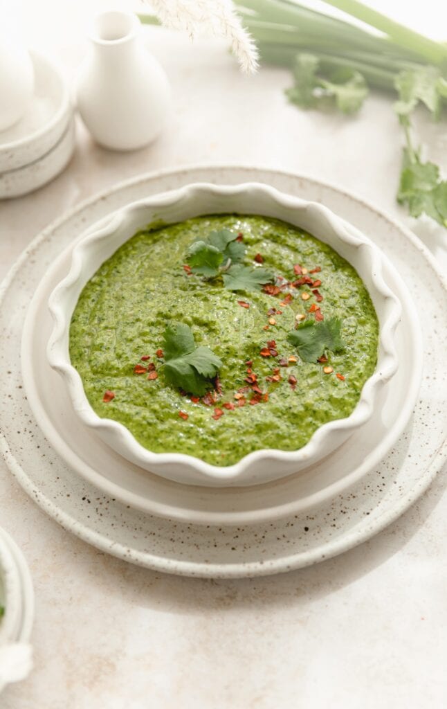 Scalloped edge white bowl full of chimmichurri sauce with red pepper flake garnish 
