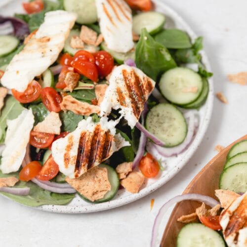 white plate with a sliced of grilled Halloumi on mixed greens