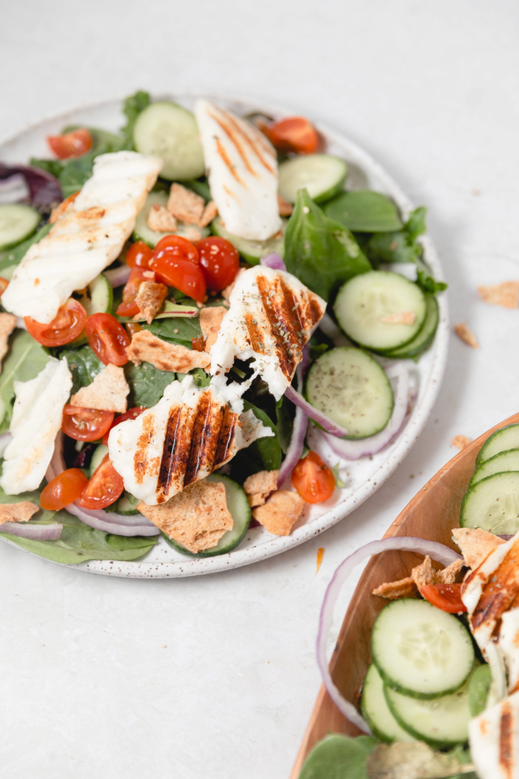 a piece of grilled Halloumi cheese pulled in half on a mixed greens salad
