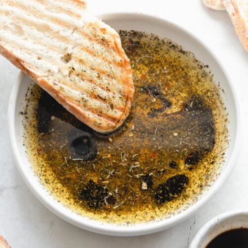 white bowl with bread dipping oil and crusty bread dipping in it