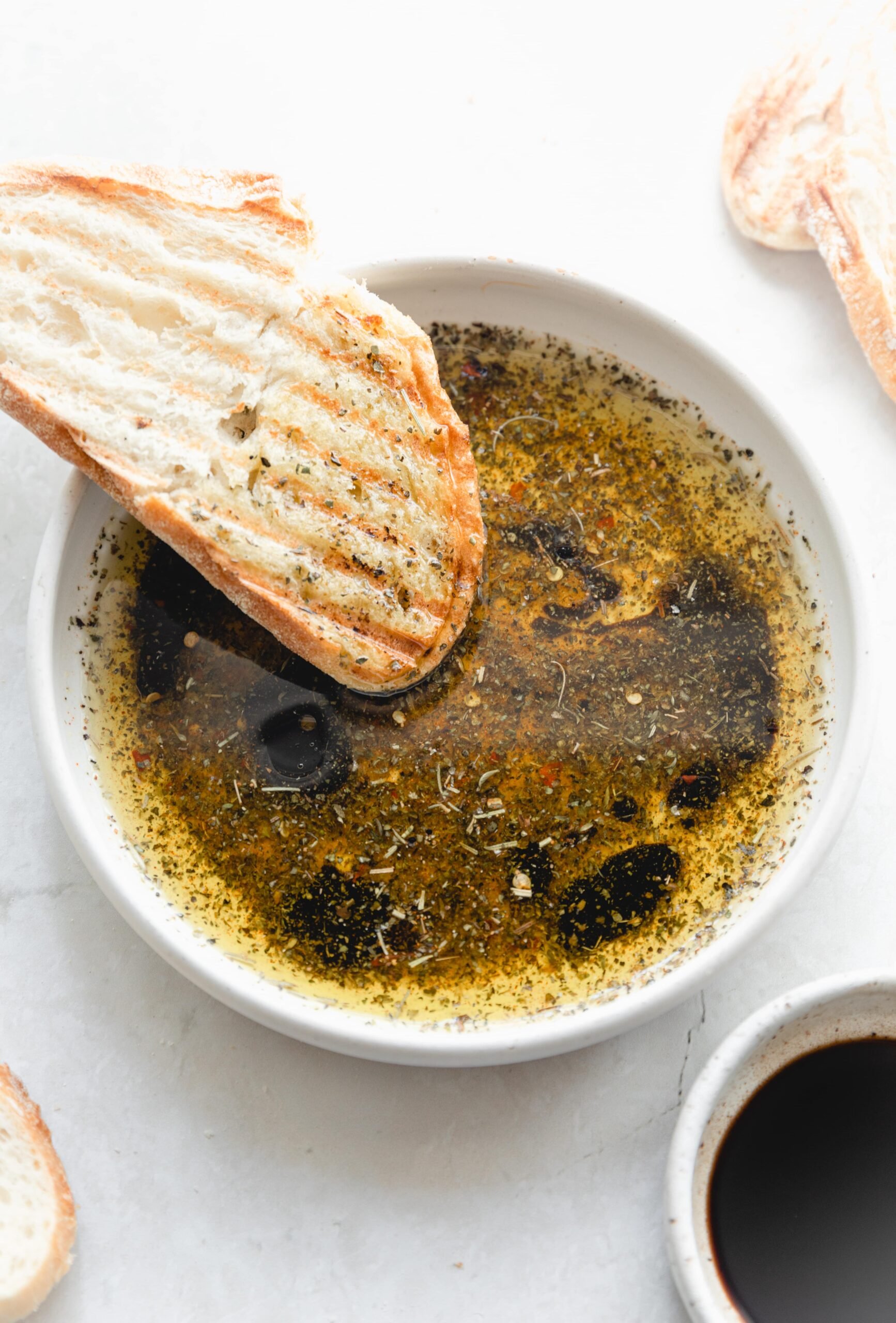 white bowl with bread dipping oil and crusty bread dipping in it