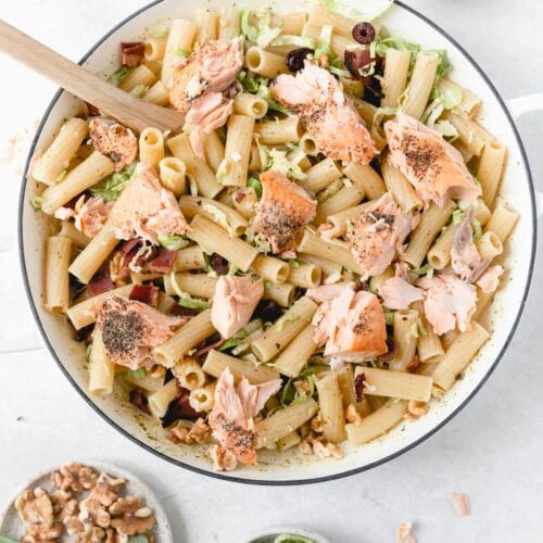 white skillet with pesto pasta topped with salmon