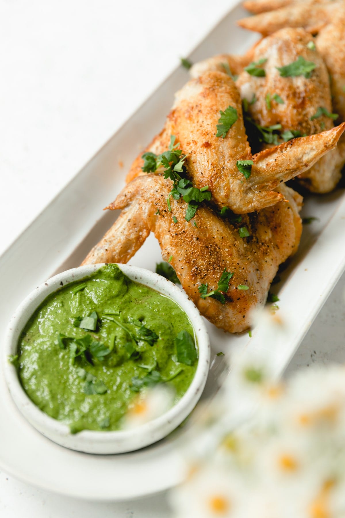 Crispy air fried wings on a white plate with chimmichurri sauce
