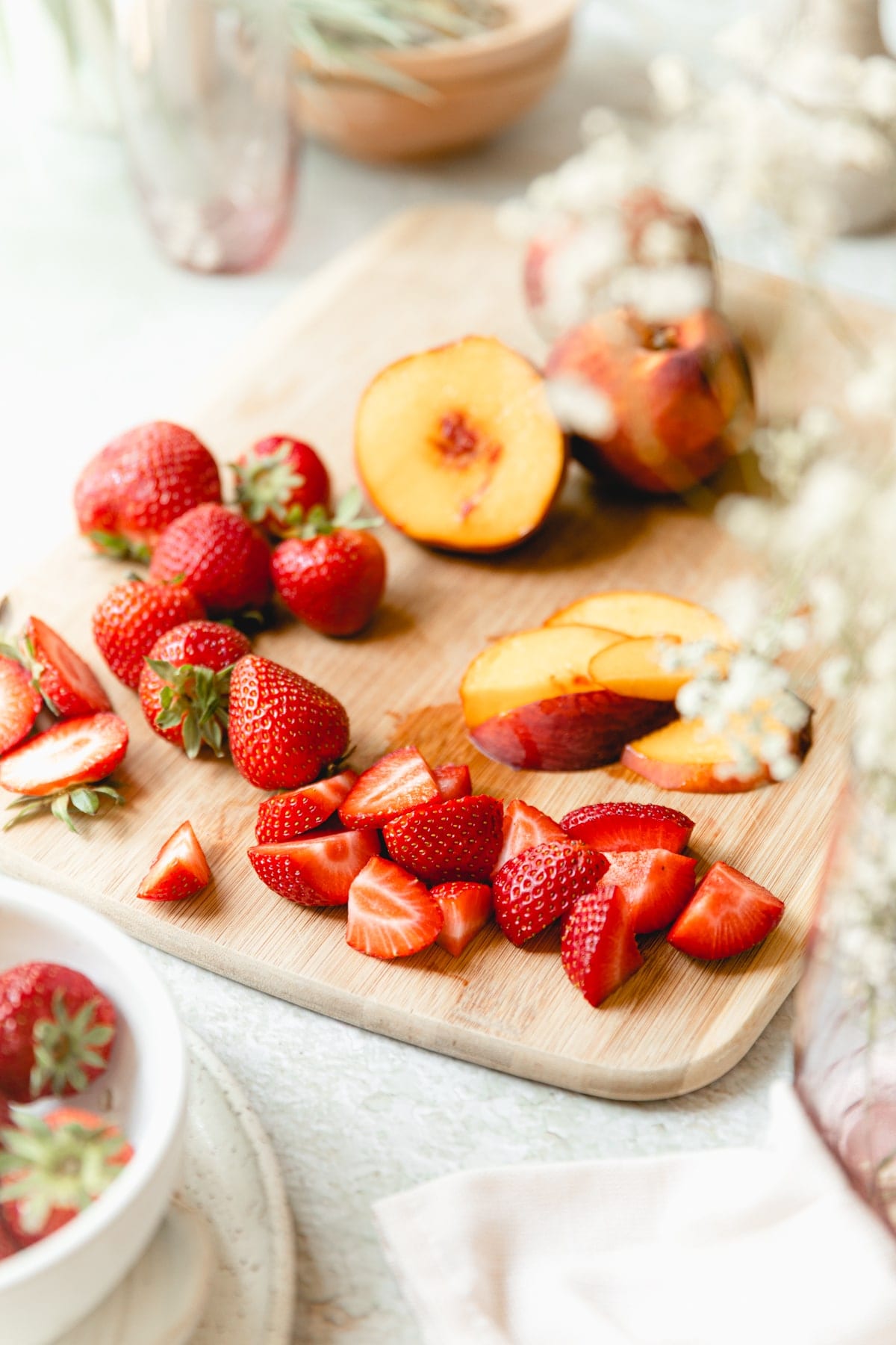 cut strawberries and peaches on a wooden cutting board 