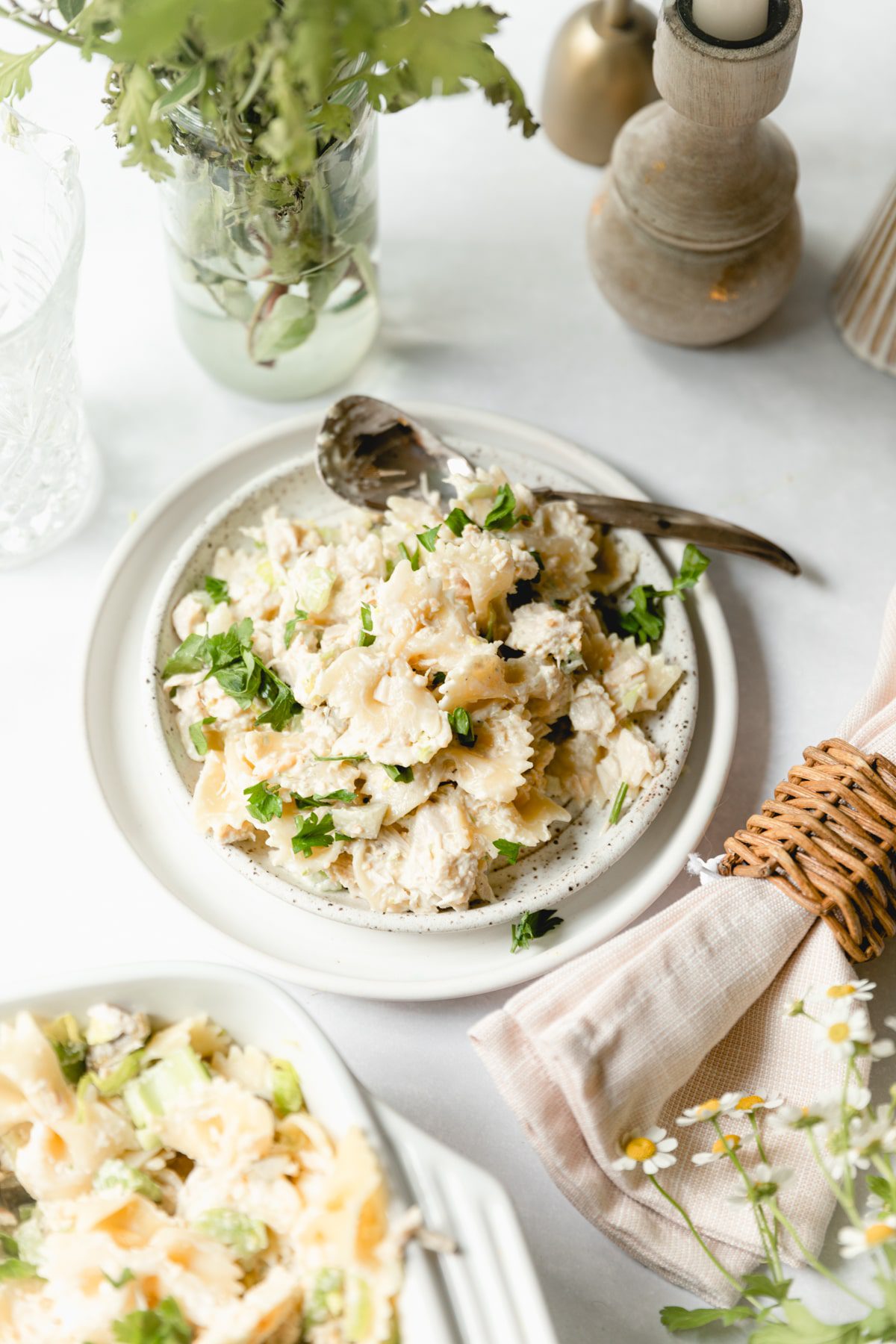 white plate with a serving of tuna pasta salad surrounded by fresh flowers 
