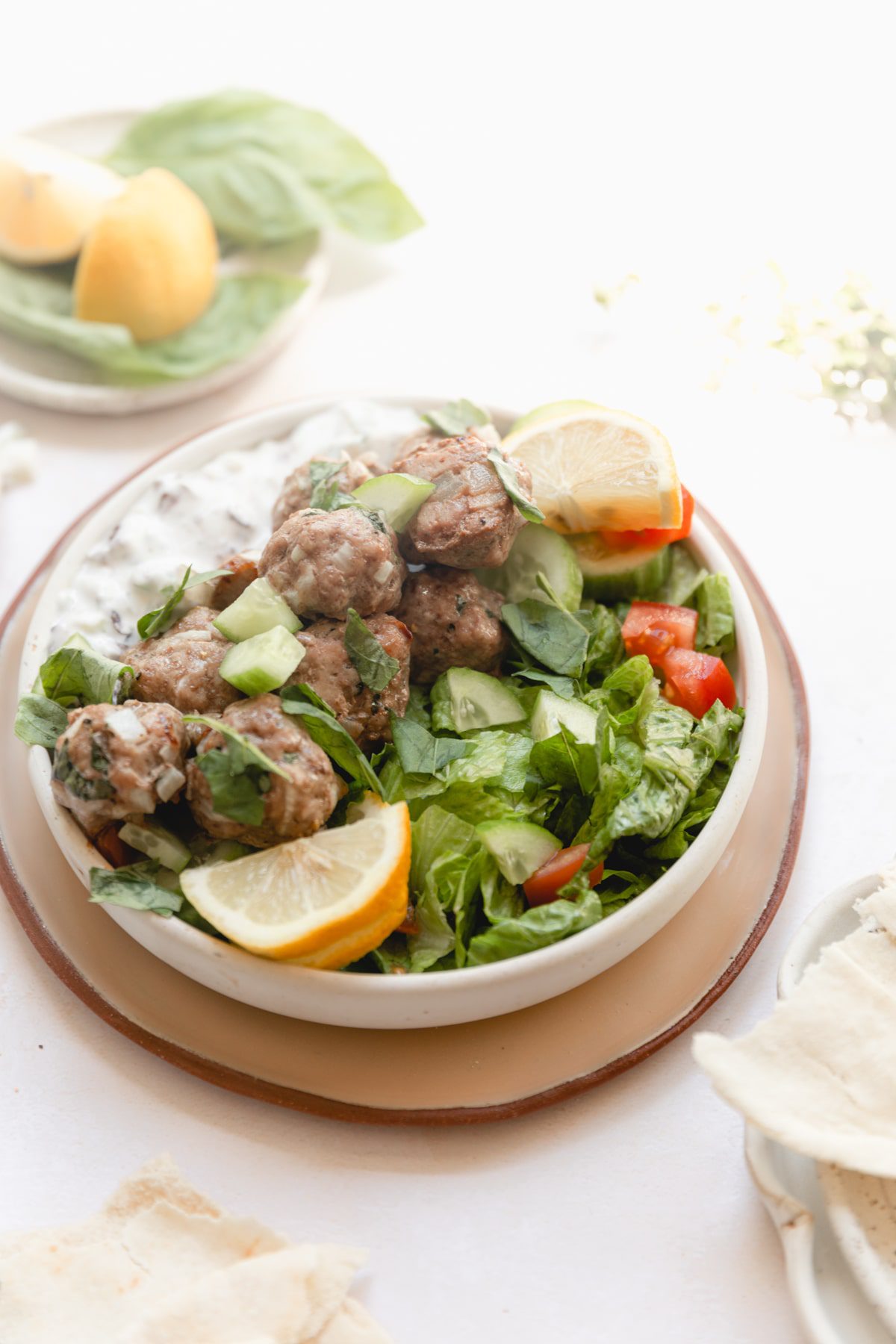white bowl of salad topped with lemon basil greek meatballs 
