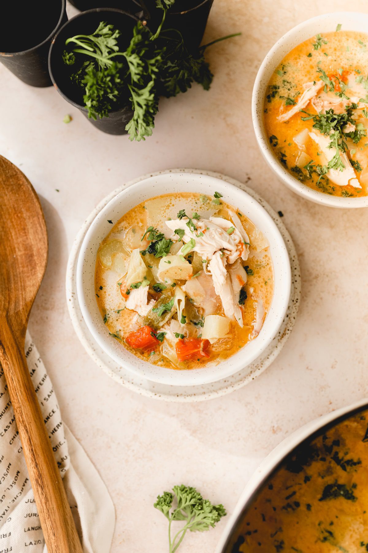 white bowl with chicken potato chowder next to a wooden spoon
