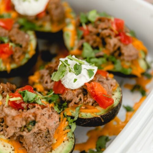 baked avocados in a white baking dish topped with sour cream and cilantro