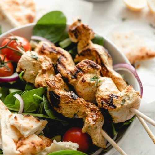 chicken on skewers placed on a salad