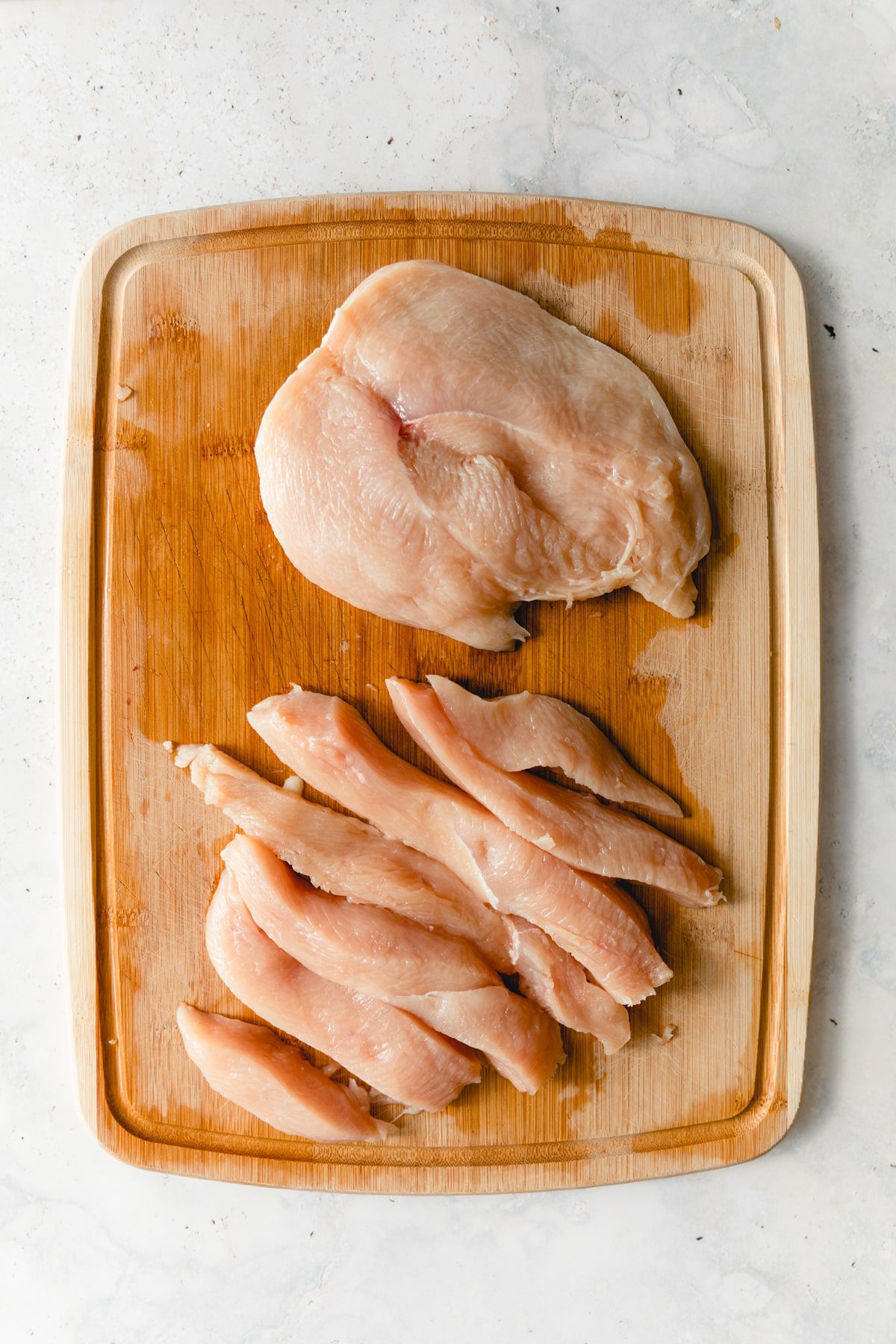 one butterfly sliced chicken breast and one sliced chicken breast on a cutting board