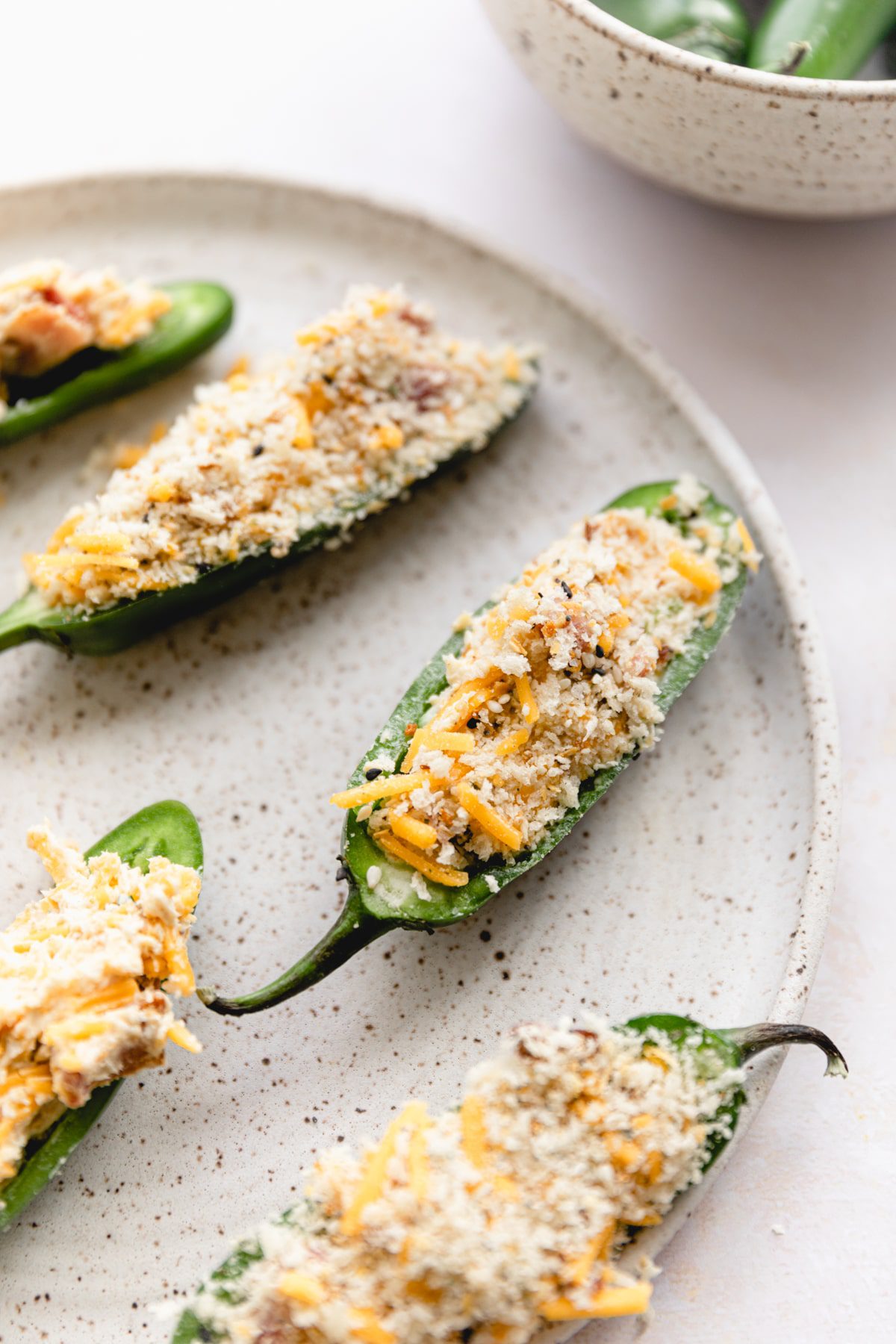 jalapeños stuffed with cream cheese and topped with breadcrumb topping on white plate