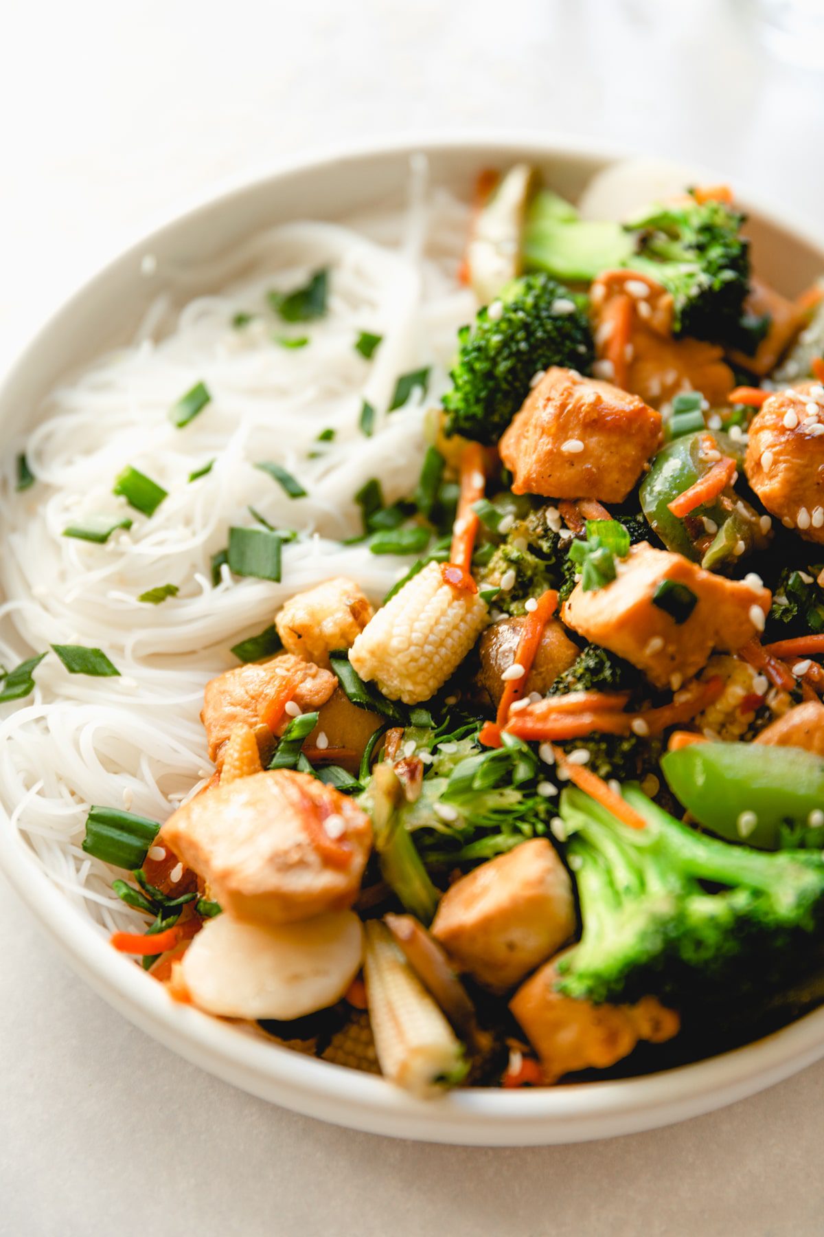 close up photo of chicken stir fry served with rice noodles in a white bowl