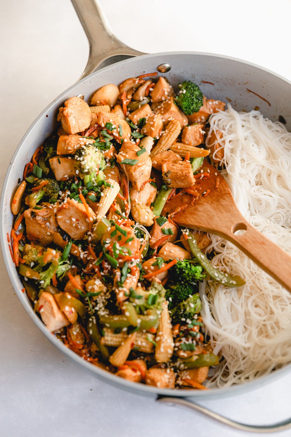 saute pan with rice noodles and stir fry in it with a wooden spoon