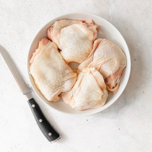 chicken thighs in a white bowl with a boning knife