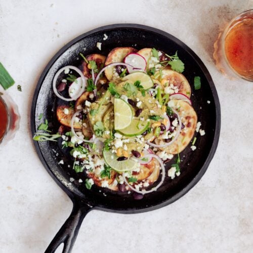 cast iron skillet with loaded potato nachos and toppings