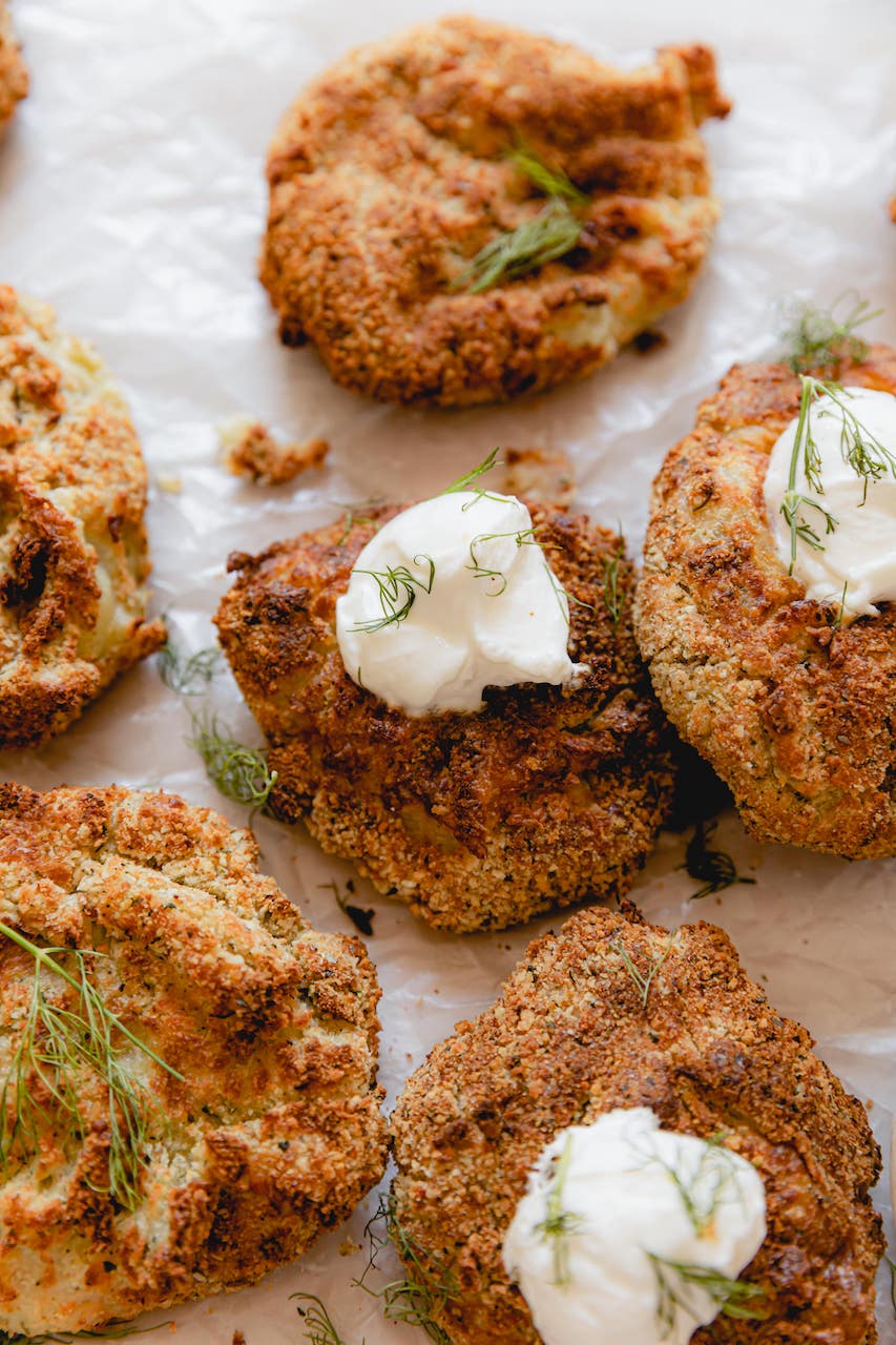 multiple potato fritters on parchment paper with dill and sour cream garnish